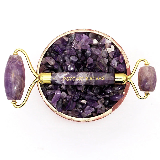 A long, detailed image of the Psychic Sisters Amethyst Facial Roller, a dual-ended gemstone massage tool designed to reduce facial and under-eye puffiness, featuring a natural amethyst gemstone with a size of 6x3 centimetres, presented in a beautiful gift box