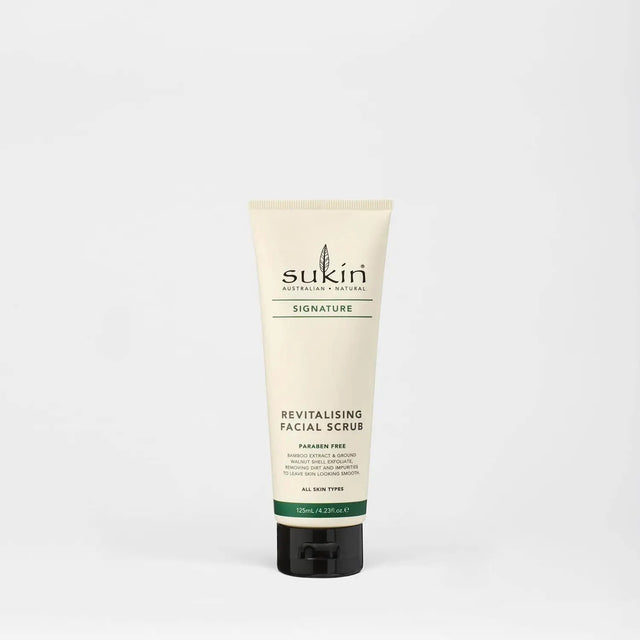 A close-up of Sukin Revitalising Facial Scrub in a 125ml tube, showcasing its creamy texture with gentle bamboo and walnut shell granules, surrounded by natural ingredients like aloe vera, chamomile, sesame oil, and rosehip oil to highlight its exfoliating and hydrating properties